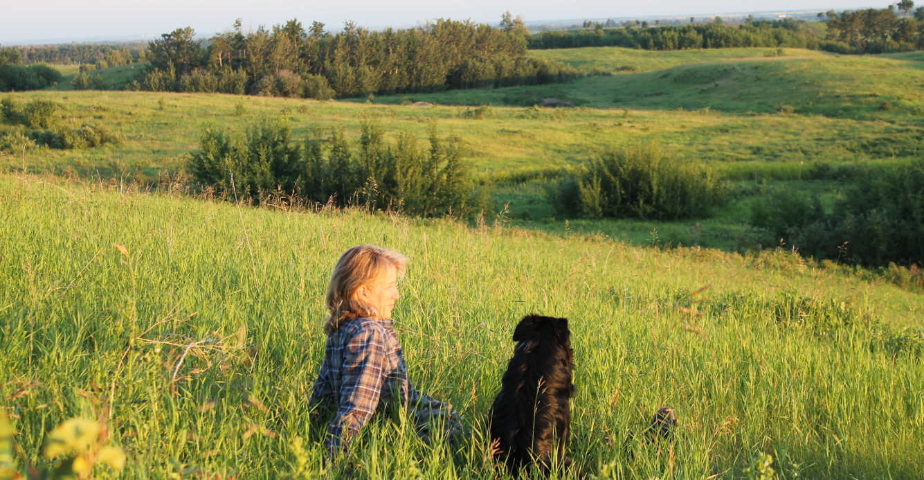 Image of Sara and her dog hudson sitting on a beautiful green hillside at Wildeflower Bride Farms